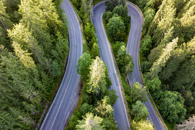 Aerial view of winding road in high mountain pass trough dense trees, meant to illustrate mapping your customer journey.