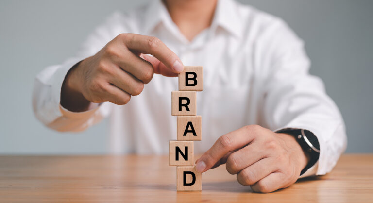 Businessman balancing building blocks in a stack that spell BRAND.