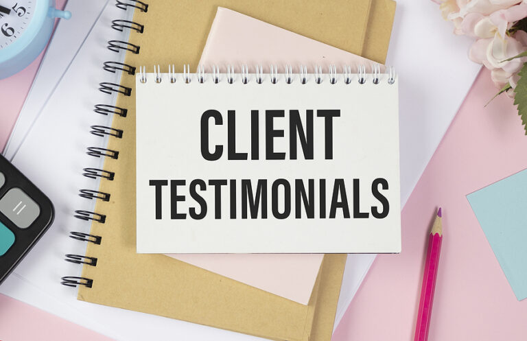 "Client Testimonials" written on a notepad on top of a pick desk cluttered with notebooks.