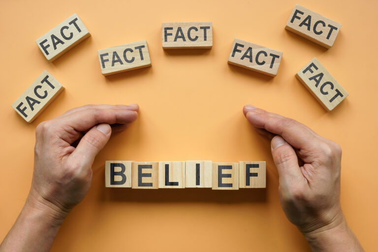 Hands shield "belief" written in wooden blocks from several "facts" written in wooden blocks as a representation of confirmation bias.