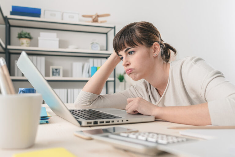 Tired disappointed woman working at office desk with a laptop.