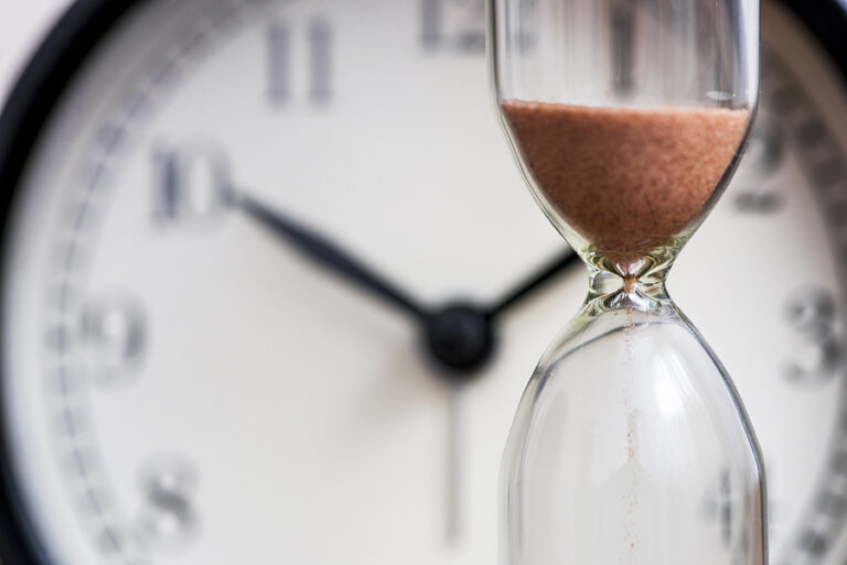 An hourglass in front of a clock meant to signify better time management