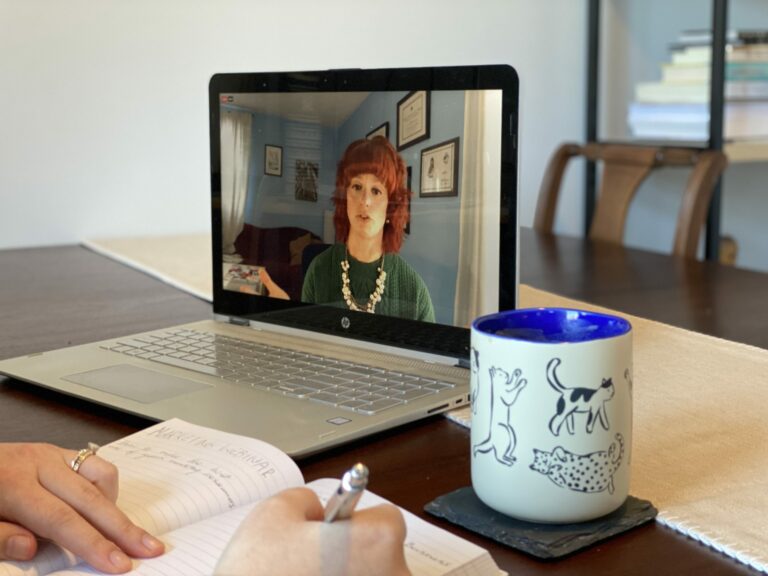 A picture of Vision COO Julia Becker Collins presenting a Business Bootcamp webinar on the screen of alaptop on top of a desk, where someone is taking notes in a notebook