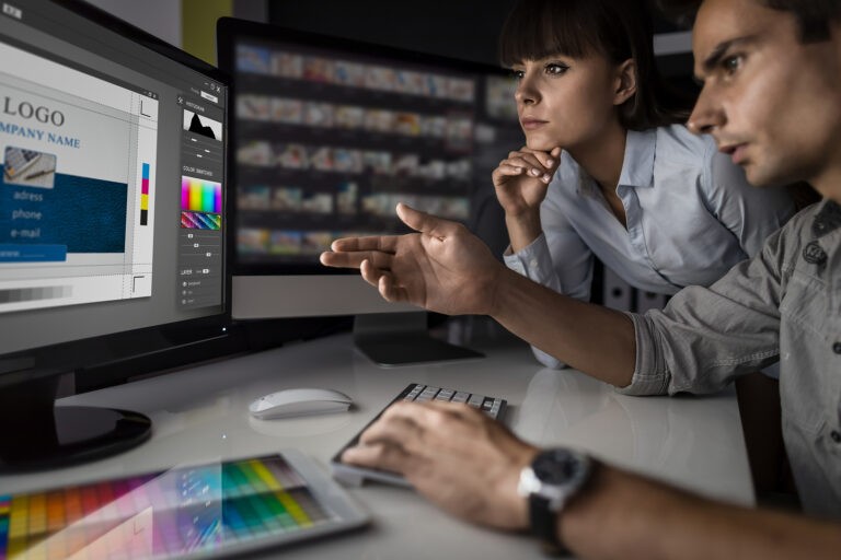 Graphic Designers discuss changes to logo and branding in front of computer.