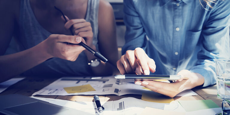 Two business owners reviewing business strategy with printouts and a tablet.