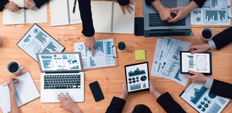 People in a marketing department look over laptops, tablets, and printouts of marketing analytics.