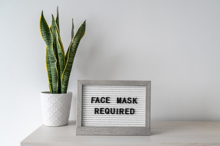 A sign on top of a table next to a plant that reads "Face Mask Required"