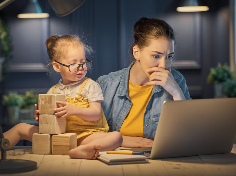 Young mother with toddler child working on the computer from home at night.