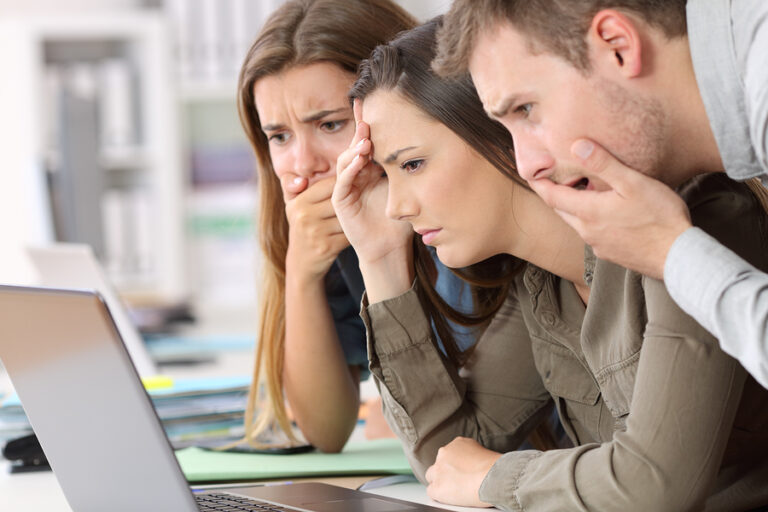 Three employees looking at a laptop unhappily.