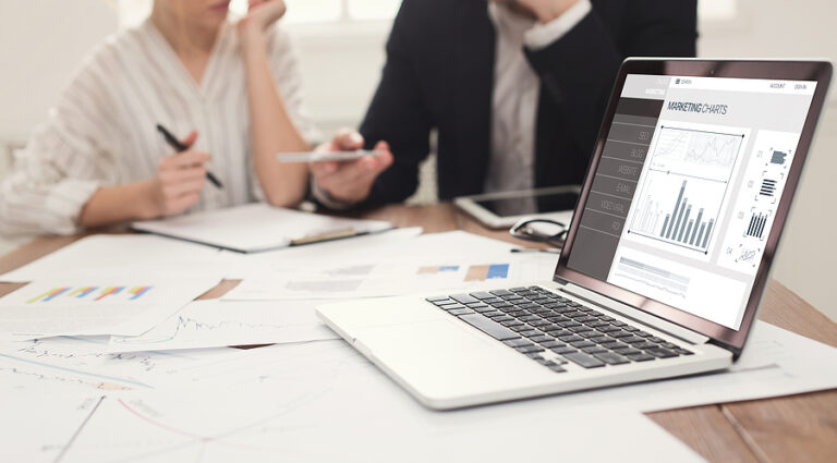 Two business people consult over graphs with a laptop in the foregrounf with a chart graphic.