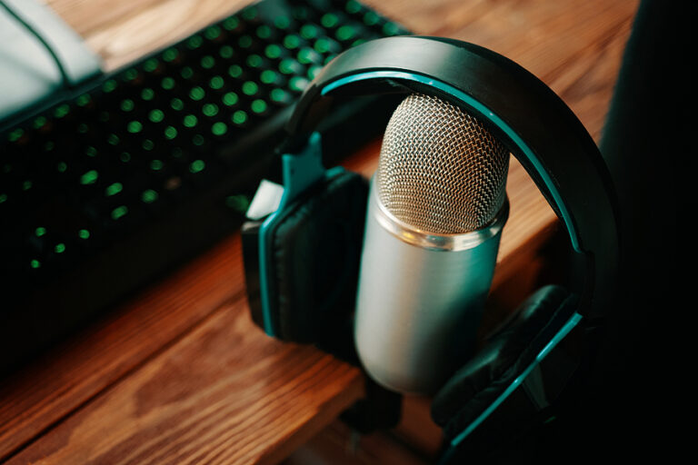 A pair of headphones draped over a microphone on top of a desk next to a keyboard, meant to signify marketing with podcasts.