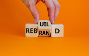 Orange background with a hand that is turning the central block of three blocks so that it reads rebrand.