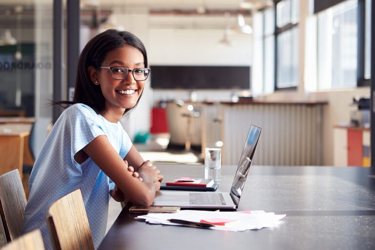 Young woman in office with laptop smiling.