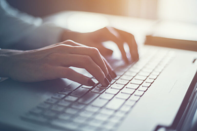 Woman's hands typing on a laptop keyboard in subdued lighting.