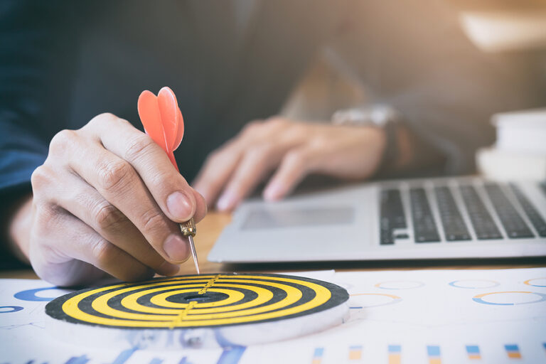 Man with laptop targeting a bullseye with a dart.