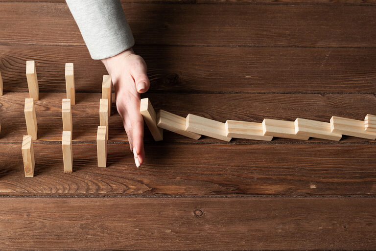 A business woman using her hand to some a line of dominoes from tipping over a large grouping of dominoes on a wooden desk, meant to portray crisis management for businesses