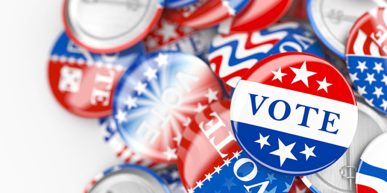 A pile of red, white, and blue voting pins, meant to relate to politics and voting in the workplace